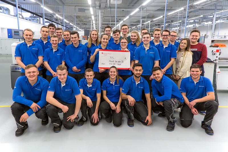 28 apprentices from MAPAL present a large donation cheque. They are at the MAPAL Training Centre.