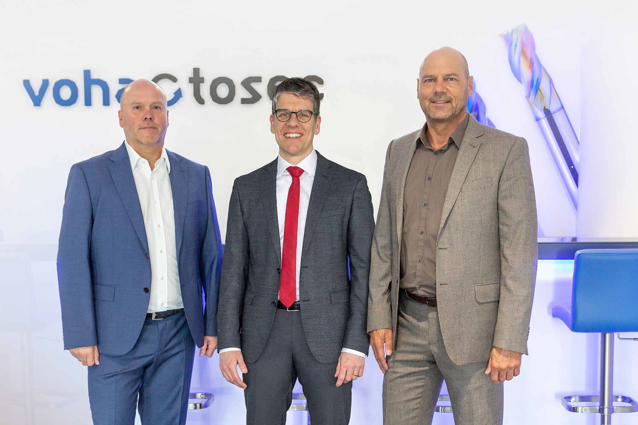 Dieter Scheurer, Dr Jochen Kress and Carsten Klein stand in front of the voha-tosec logo.