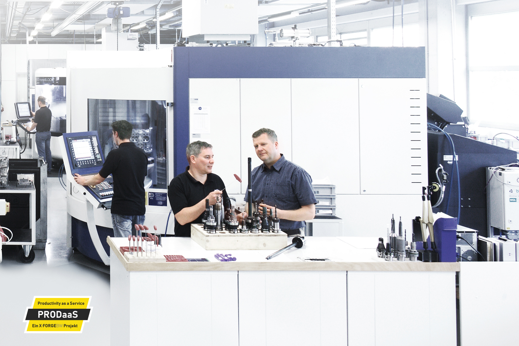 Two employees discuss the properties of various tools while other employees make adjustments to machines in the background.