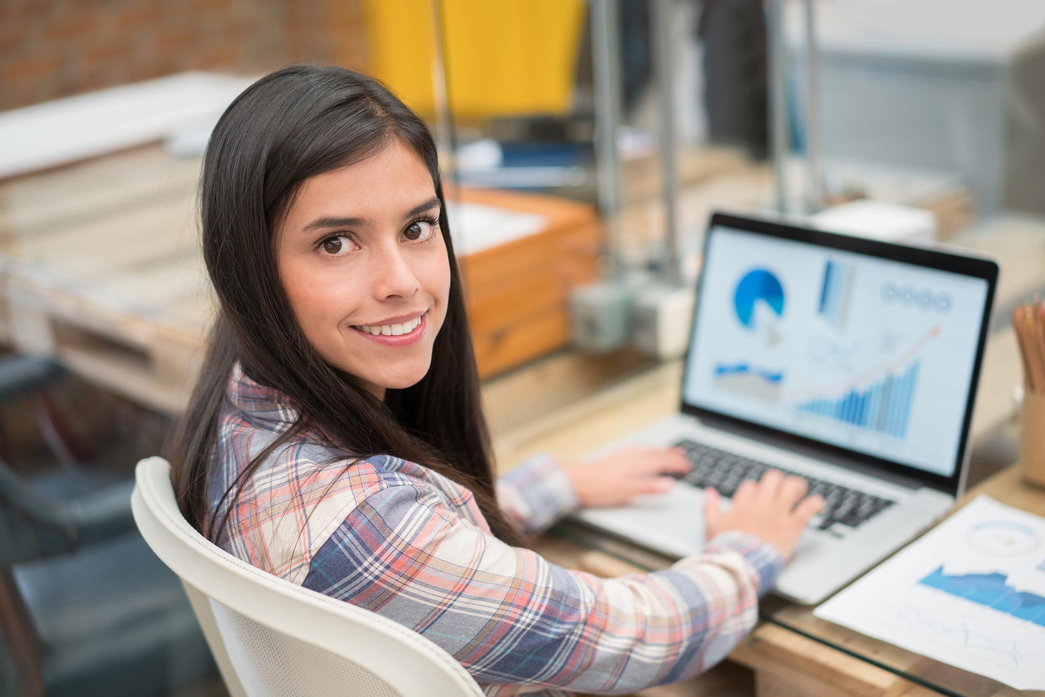 Eine junge Frau sitzt am Arbeitsplatz und blickt nach hinten in die Kamera.
