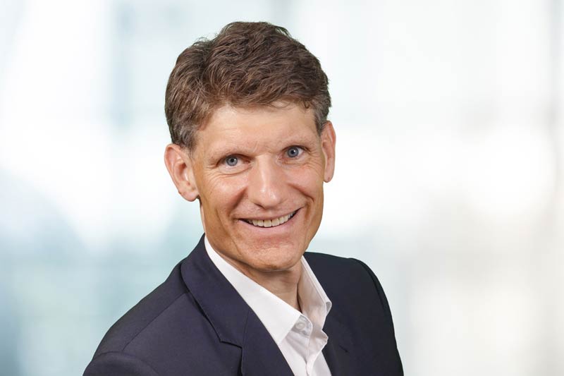 A portrait photo of Matthias Cöster. He is wearing a blue jacket and a white shirt.