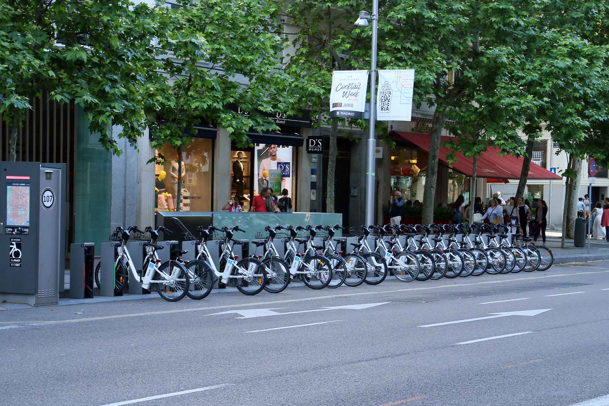 Auf einer Straße stehen in einer Reihe E-Bikes an Ladestationen.
