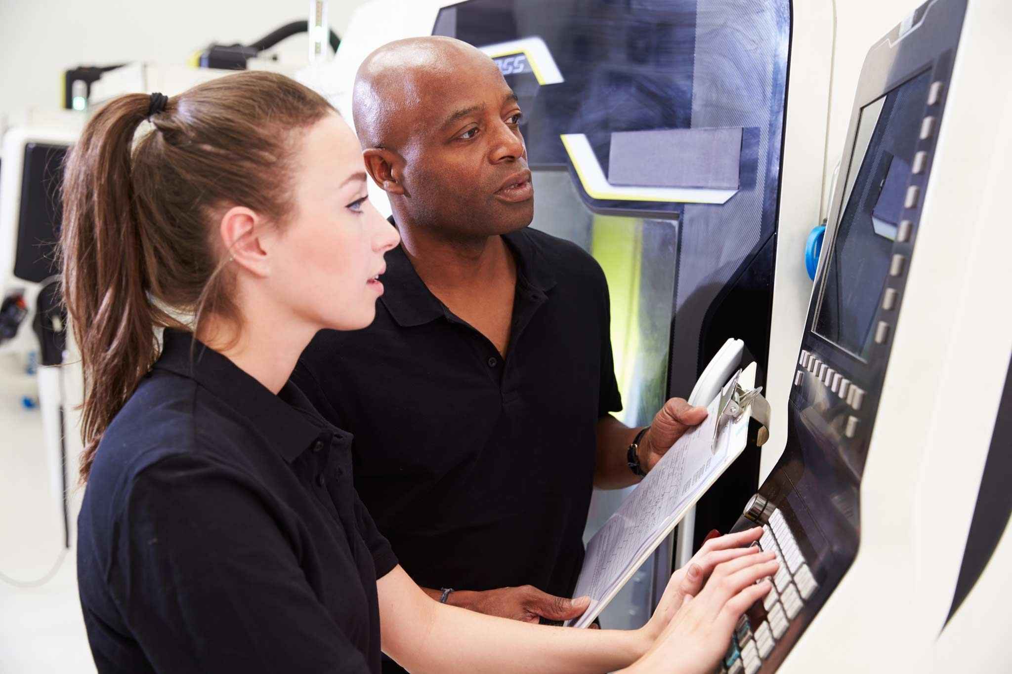 Das Bild zeigt einen Ausbilder und eine gewerblich-technische Auszubildende an der Maschine.