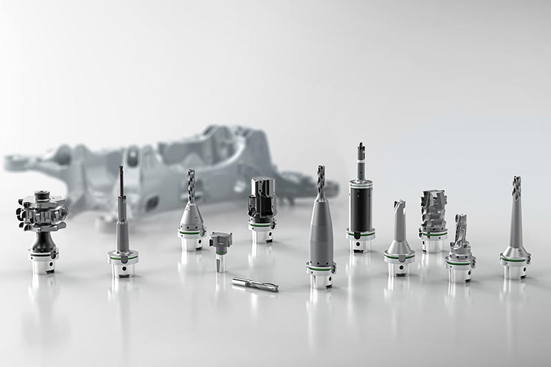 Twelve tools for complete machining are placed in front of a structural part, which is shown as blurred in the background.