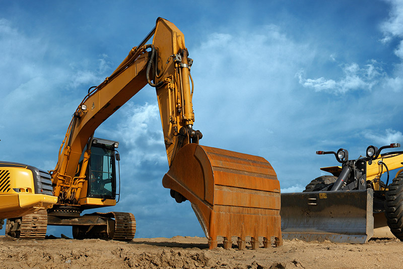 The picture shows a yellow excavator against a blue sky.