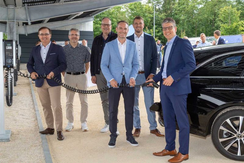 Eine Gruppe von Männern hält das Ladekabel eines Elektroautos in der Hand. Im Hintergrund eine Carport-Photovoltaikanlage.