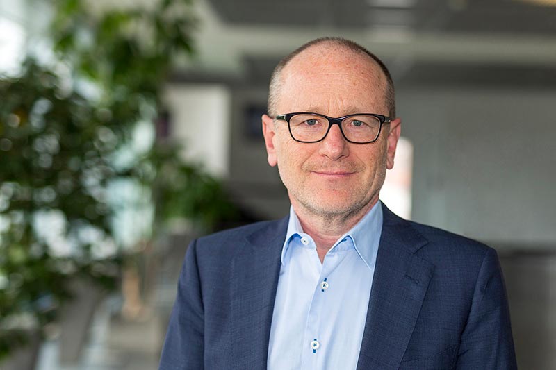 A portrait of Jacek Kruszynski, wearing glasses, a light blue shirt and a dark jacket.