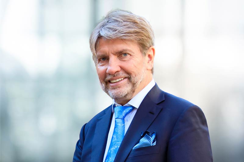 A man with a short beard, dark blue jacket, light blue tie and pocket square