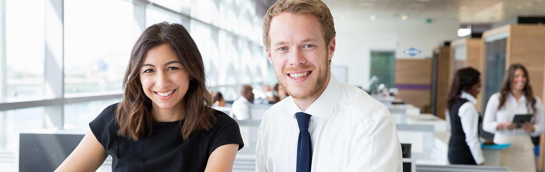 Two young employees smile at the camera.