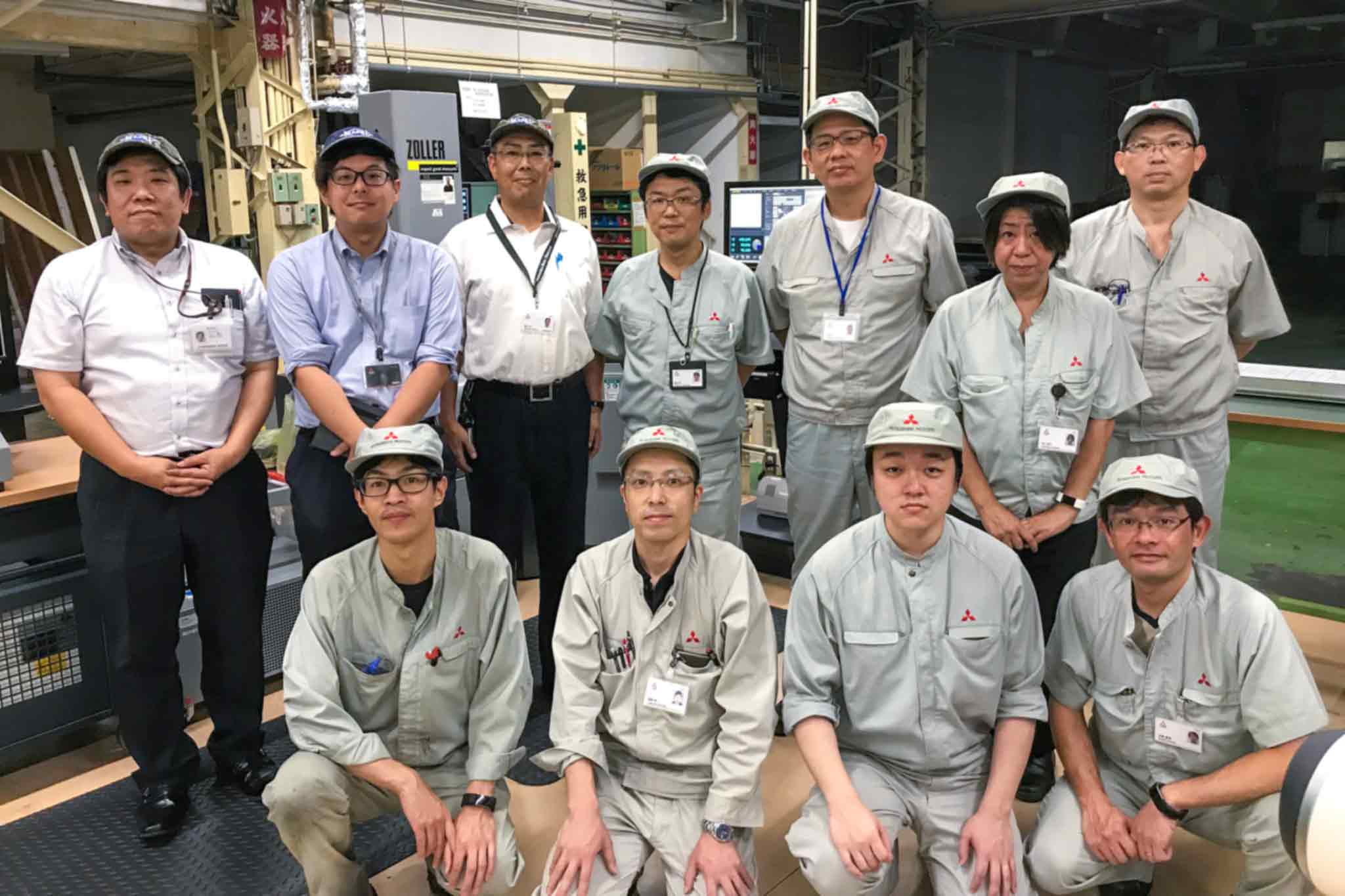 The teams from MMC and MAPAL, a total of eleven people, stand in front of a machine in the manufacturing area.