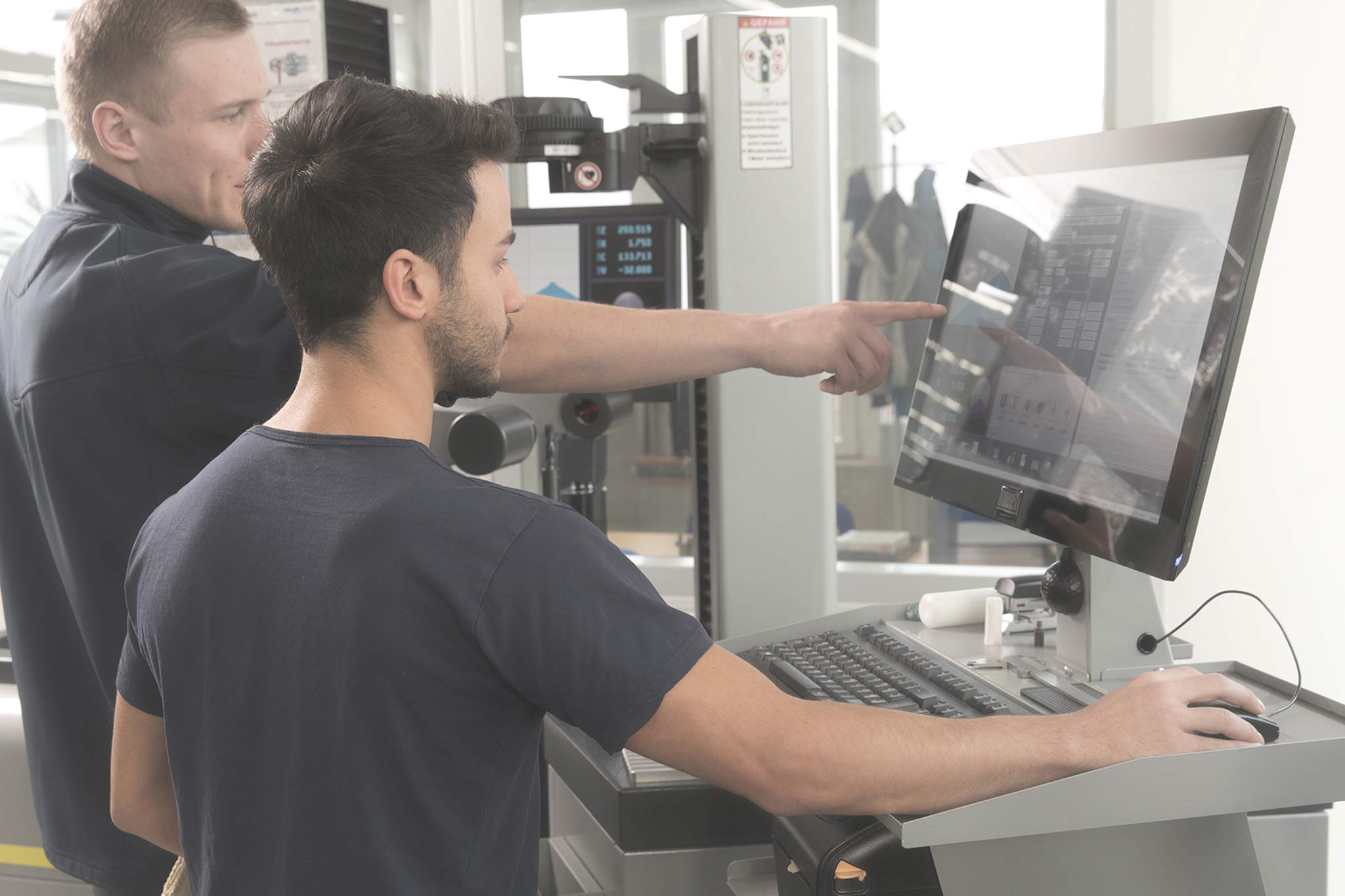 Das Bild zeigt einen jungen Mann in der Produktion mit einem Produktionsmitarbeiter.