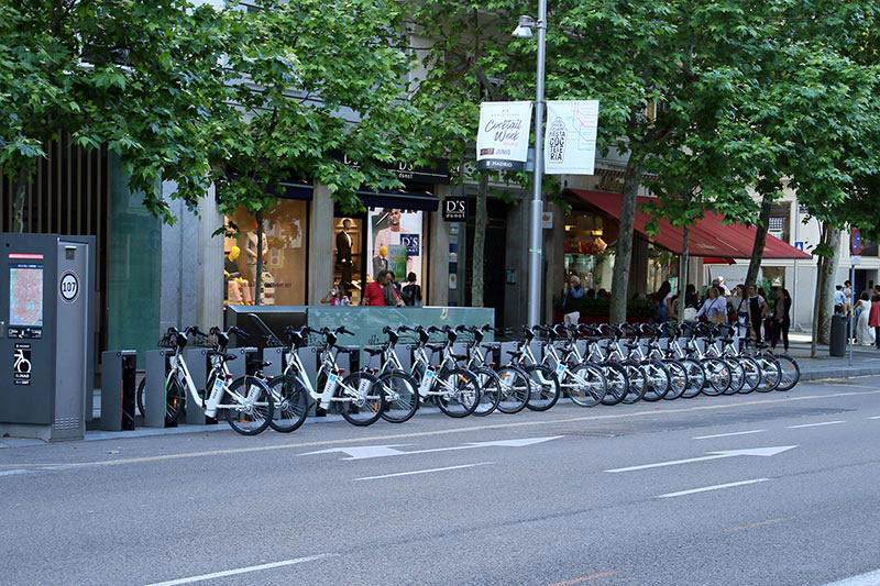 There are e-bikes in a row at charging stations on a street.